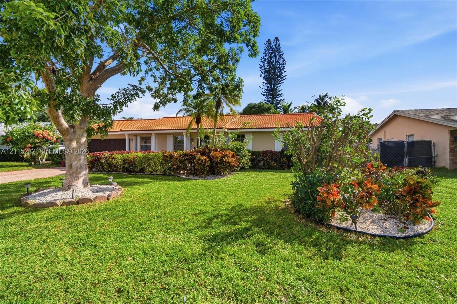 Single-story residence featuring a terracotta-tiled roof, manicured lawn, and established landscaping with mature trees