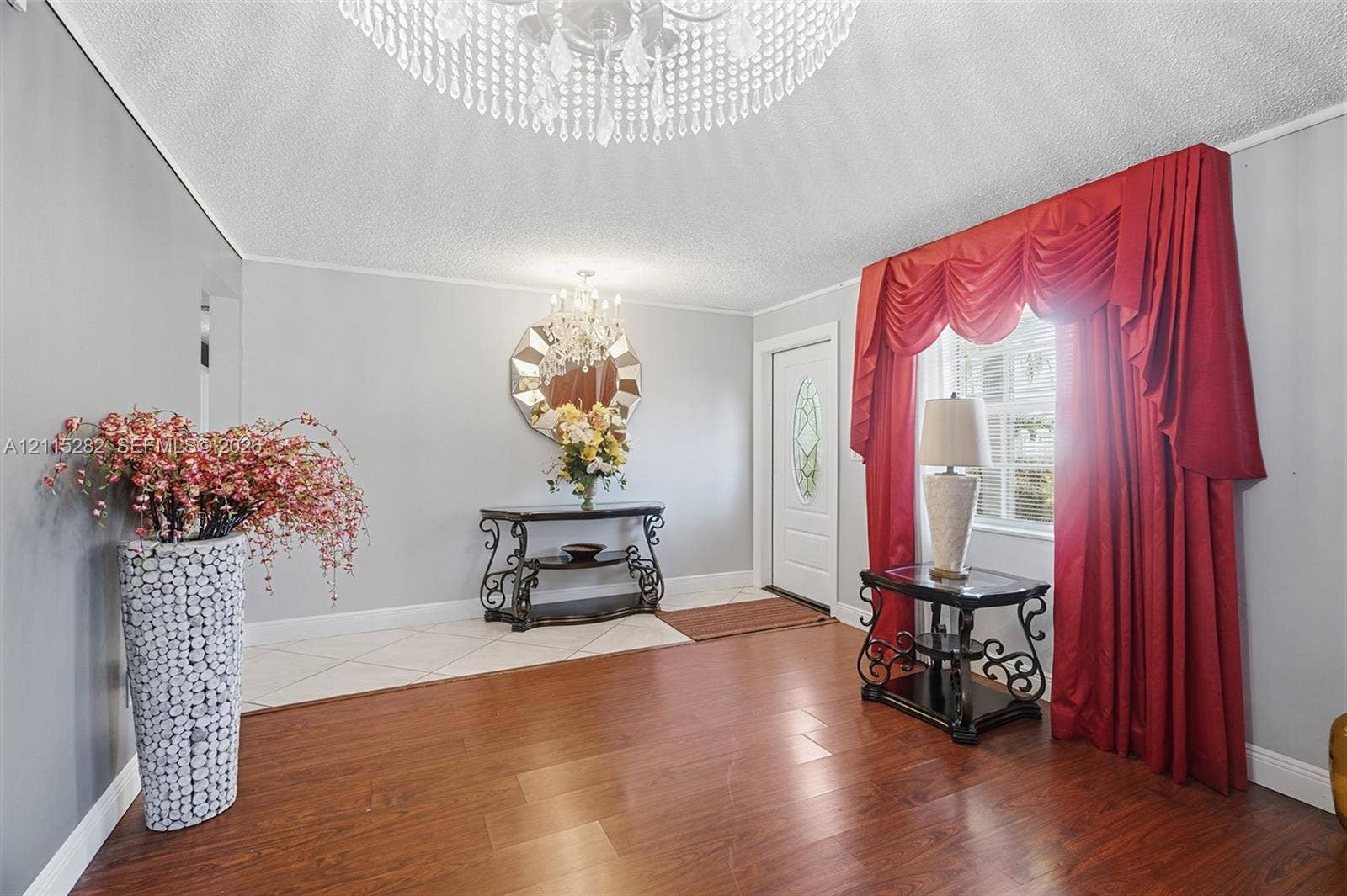 Entryway featuring wood-finish flooring, diamond-pattern tile inlay, decorative crystal chandeliers, and an exterior door with a leaded glass insert