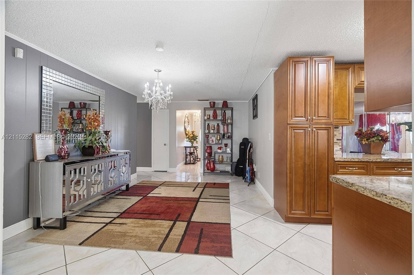 Open-concept interior featuring large-format ceramic tile flooring, wood cabinetry, stone countertops, and a ceiling-mounted crystal chandelier