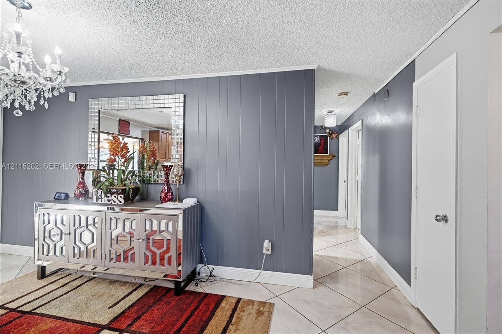 Grey vertical paneling, ornate crystal-style chandelier, and diamond-set ceramic tile flooring