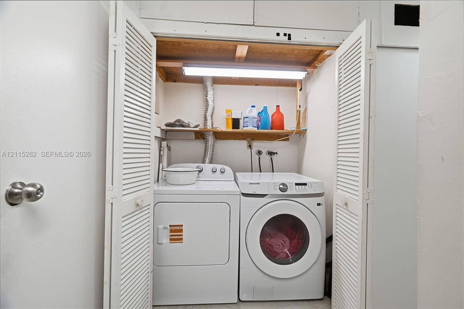 Laundry area featuring louvered bifold doors, overhead lighting, and built-in wooden shelving