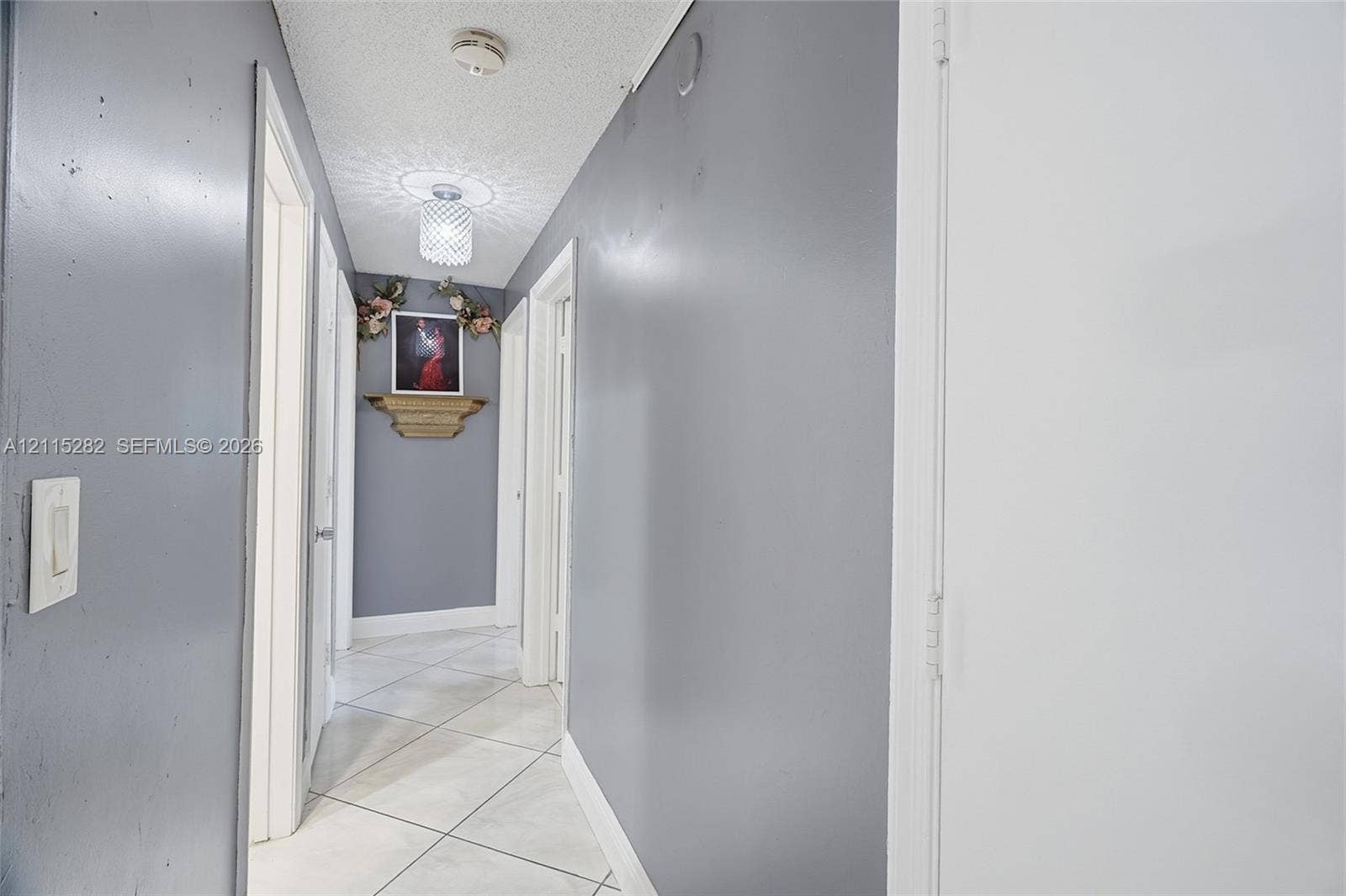 Neutral-toned hallway featuring large-format diagonal tile flooring, smooth-finish walls, and decorative ceiling-mounted lighting