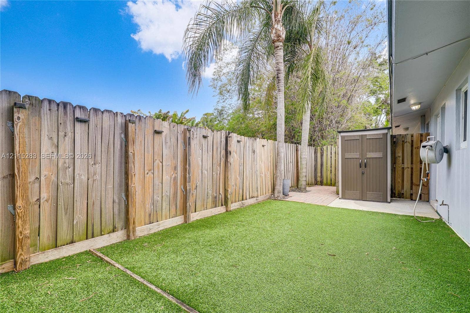 1619a NE 25th Street, #A, Wilton Manors, Wilton Manors, FL 33305 Private side yard featuring a wood privacy fence, artificial turf, brick-paver patio area, and mature palm trees