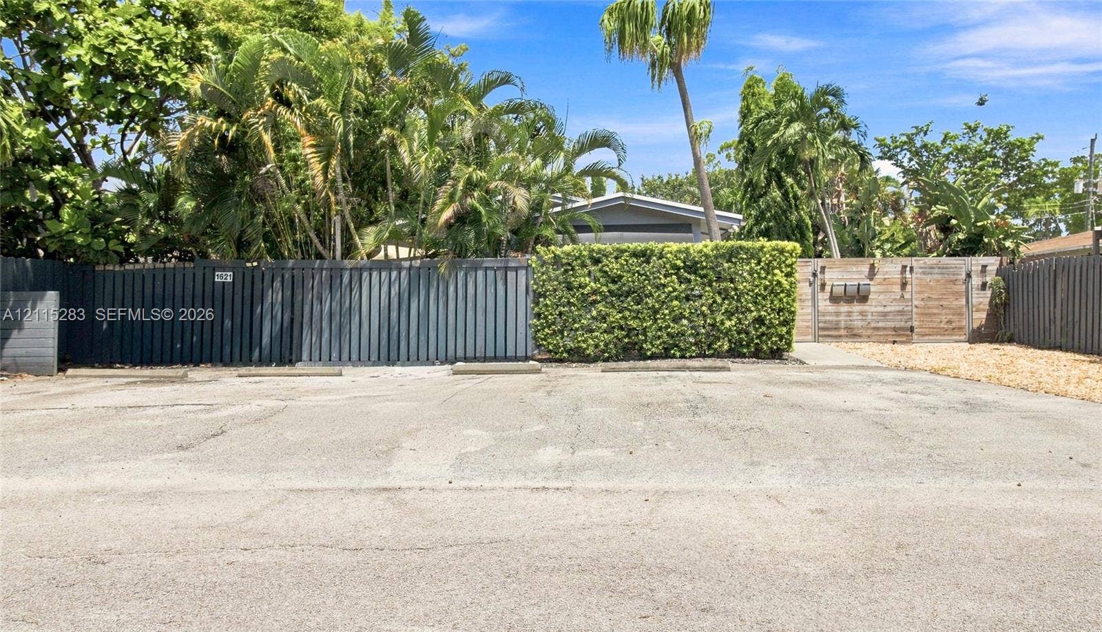 1619a NE 25th Street, #A, Wilton Manors, Wilton Manors, FL 33305 Paved off-street parking area featuring concrete wheel stops, dark-stained horizontal wood privacy fencing, and mature tropical landscaping