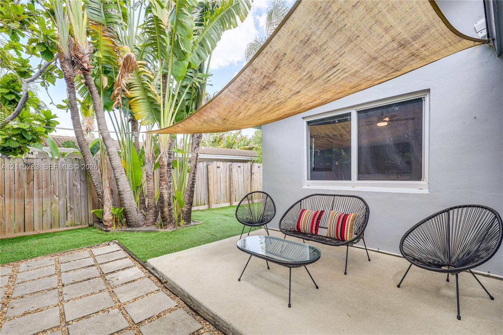 1619a NE 25th Street, #A, Wilton Manors, Wilton Manors, FL 33305 Backyard featuring a concrete patio, synthetic turf lawn, wood privacy fencing, mature palm trees, and a tension-mounted shade sail