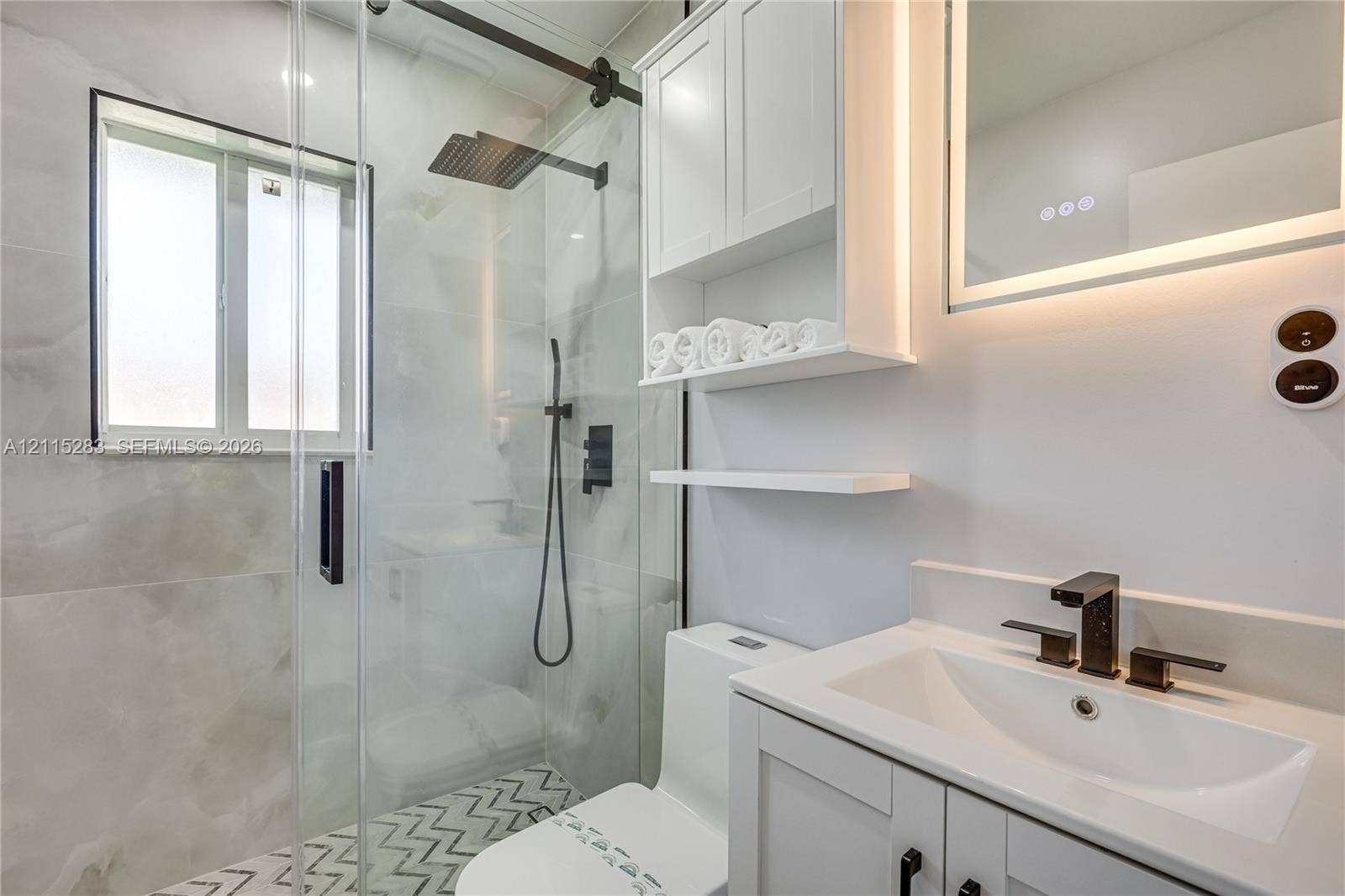 1619a NE 25th Street, #A, Wilton Manors, Wilton Manors, FL 33305 Bathroom featuring a frameless glass shower enclosure with matte black fixtures, rainfall showerhead, custom built-in white cabinetry, and geometric patterned floor tiling