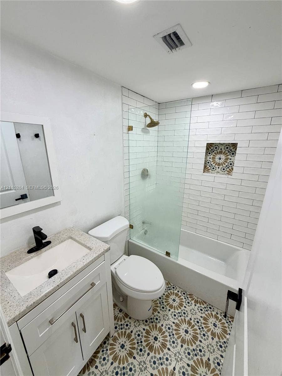 8047 NW 1st Place, Miami, Miami, FL 33150 Bathroom featuring patterned tile flooring, white subway tile shower surround with a decorative niche, frameless glass shower panel, and a stone-topped vanity with matte black fixtures