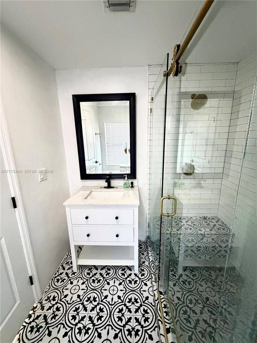 8047 NW 1st Place, Miami, Miami, FL 33150 White vanity with a stone countertop, framed mirror, glass-enclosed shower with white subway tile walls, and decorative patterned floor tiling