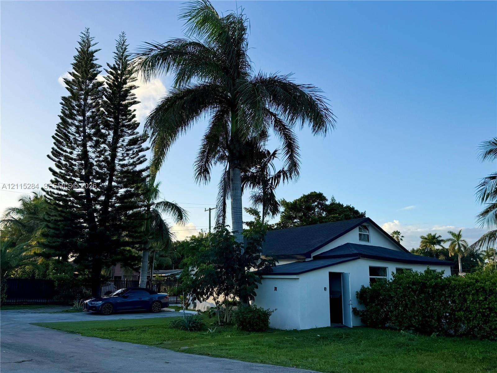 8047 NW 1st Place, Miami, Miami, FL 33150 Single-story exterior featuring a gabled roofline, light-colored smooth finish siding, and mature tropical landscaping including tall pine and palm trees
