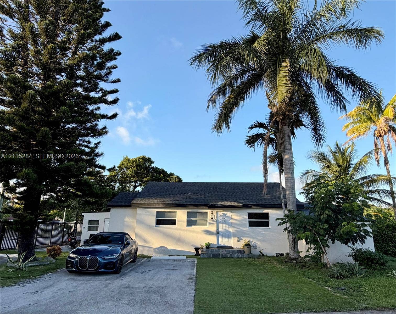 8047 NW 1st Place, Miami, Miami, FL 33150 Single-story exterior featuring a light-colored stucco facade, shingled roof, concrete driveway, and mature palm and pine landscaping