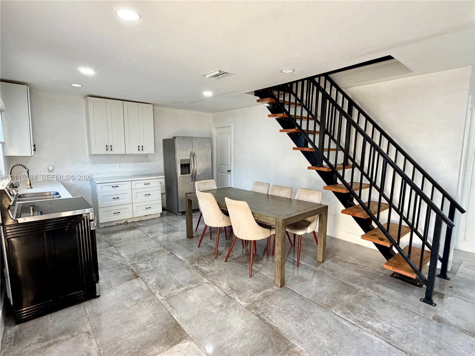 8047 NW 1st Place, Miami, Miami, FL 33150 Open-concept interior featuring large-format tile flooring, white shaker-style cabinetry, recessed lighting, and an industrial-style staircase with wood treads and black metal railings