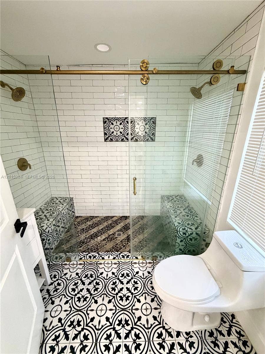 8047 NW 1st Place, Miami, Miami, FL 33150 Walk-in shower featuring a brass sliding glass door system, dual shower heads, integrated benches with patterned tile, and white subway tile surround, complemented by patterned floor tile