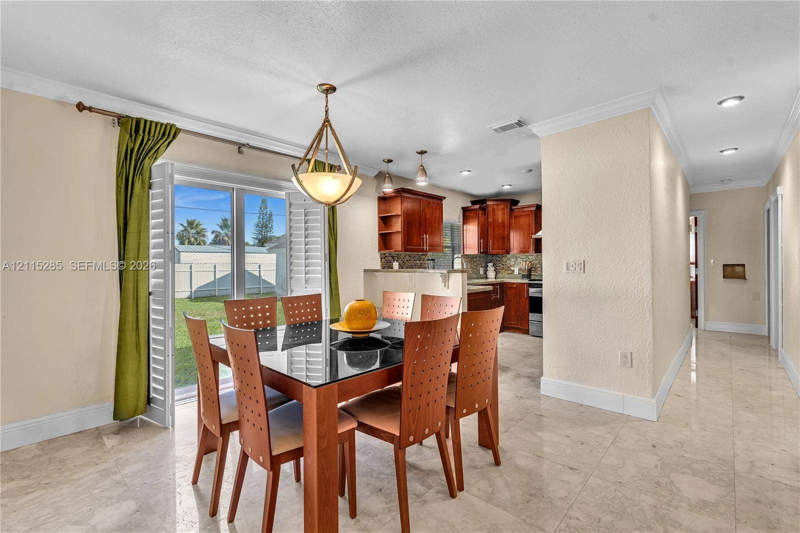 14221 Carver Drive, Miami, FL 33176 Dining area featuring stone-finish tile flooring, recessed lighting, and a geometric pendant chandelier, accompanied by a kitchen with wood-finish cabinetry and sliding glass doors