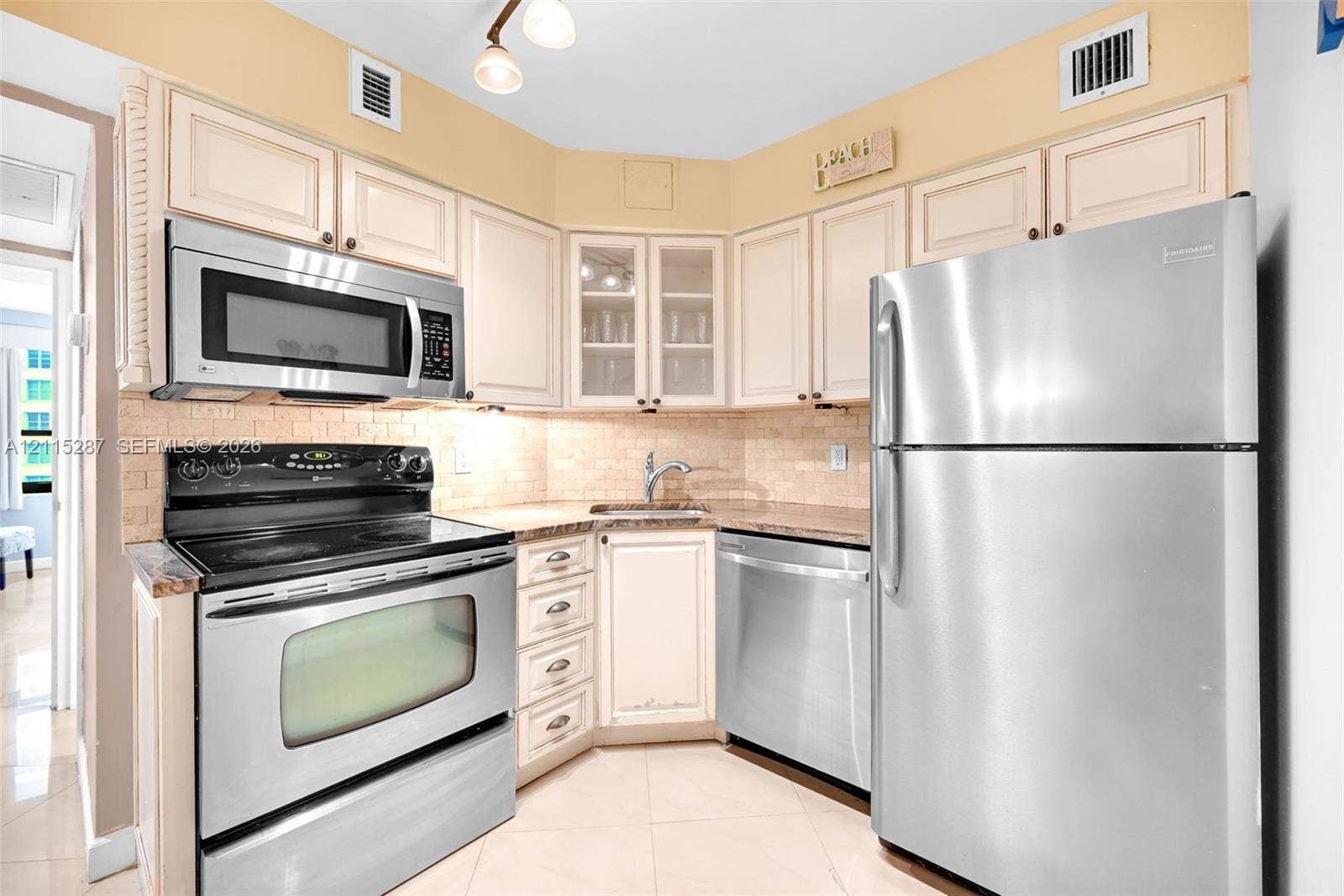 5225 Collins Avenue, #511, Miami Beach, FL 33140 Kitchen featuring stainless steel appliances, light-toned cabinetry with glass-front display panels, tiled backsplash, and stone-finish countertops