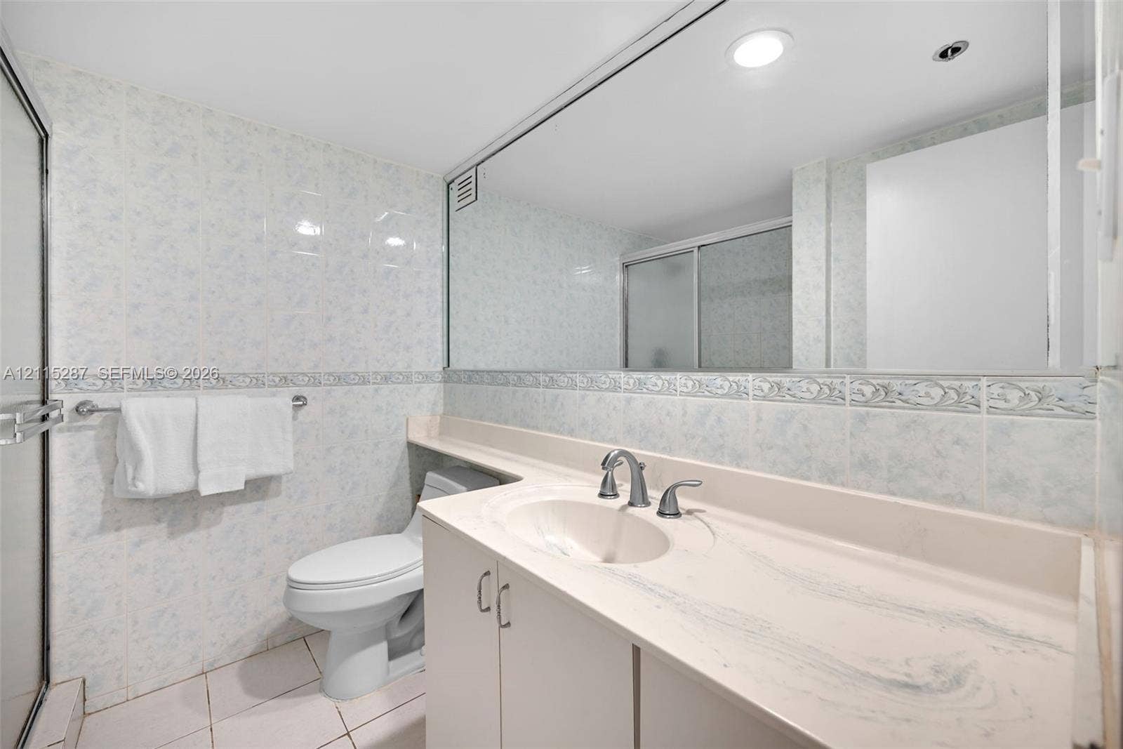 5225 Collins Avenue, #511, Miami Beach, FL 33140 Bathroom featuring wall-to-wall mirror, solid-surface vanity countertop with integrated sink, floor-to-ceiling ceramic tile, and glass-enclosed shower