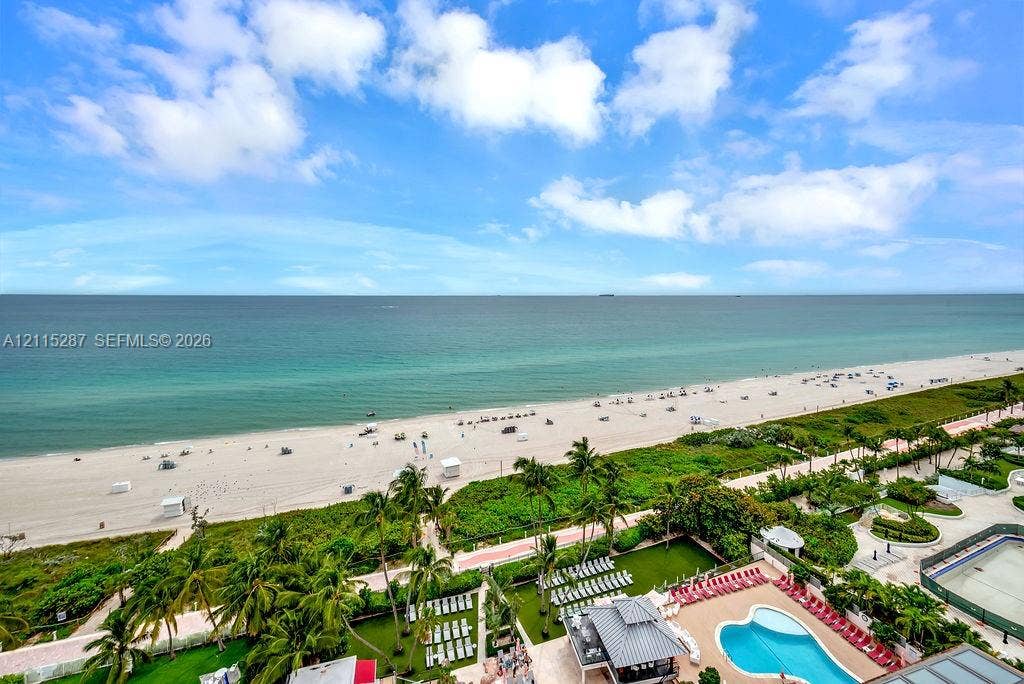 5225 Collins Avenue, #511, Miami Beach, FL 33140 Elevated oceanfront perspective featuring an expansive sandy beach, tropical landscaping, and a large custom-shaped swimming pool with surrounding terrace
