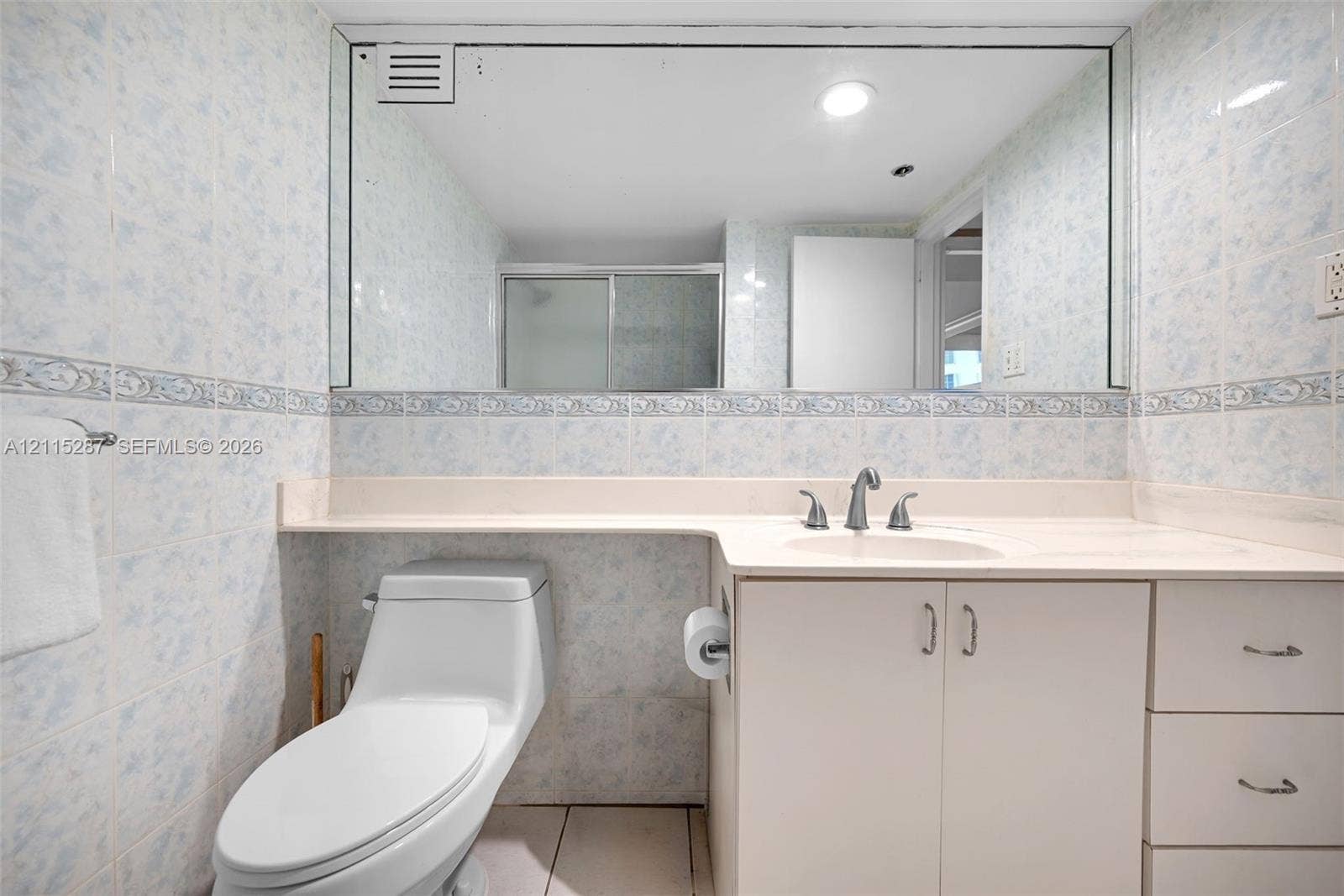 5225 Collins Avenue, #511, Miami Beach, FL 33140 Bathroom featuring a single-basin vanity with a solid-surface countertop, floor-to-ceiling tiled walls, an expansive wall-mounted mirror, and a low-profile toilet