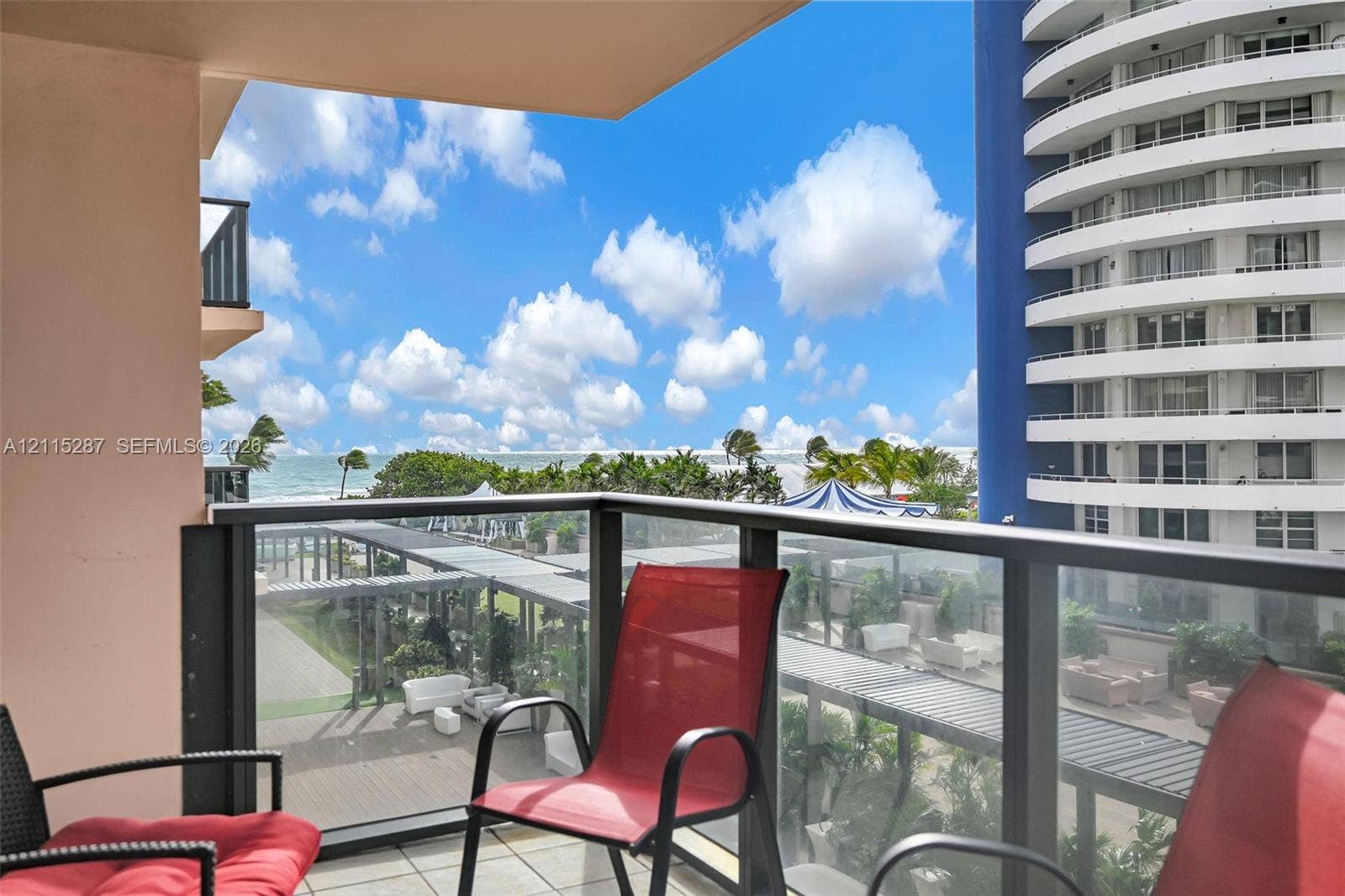 5225 Collins Avenue, #511, Miami Beach, FL 33140 Private balcony featuring glass panel railings and tile flooring, showcasing coastal scenery and palm trees