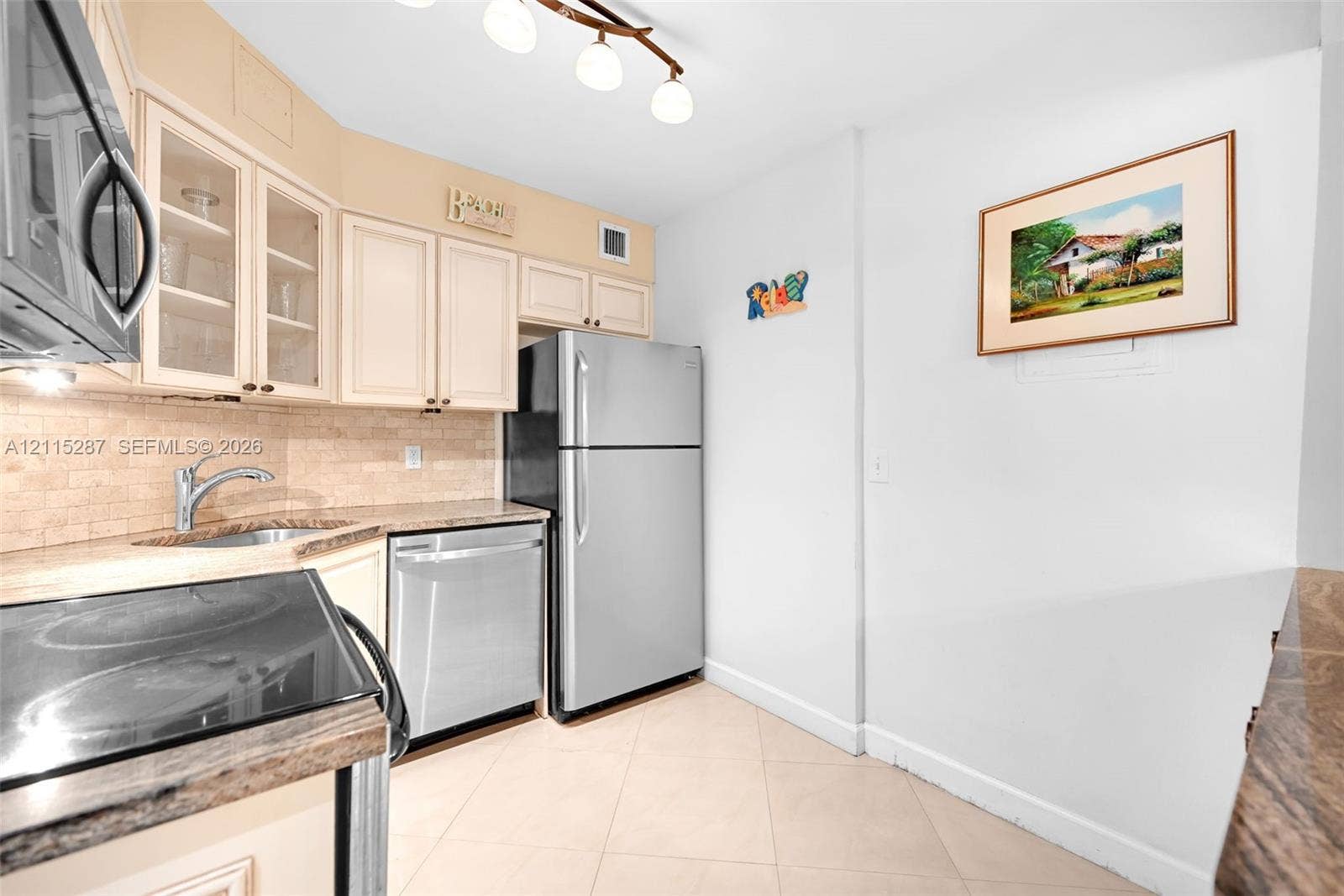 5225 Collins Avenue, #511, Miami Beach, FL 33140 Kitchen featuring cabinetry with glass-panel upper doors, stone-finish countertops, stainless steel appliances, tiled backsplash, and light-toned tile flooring