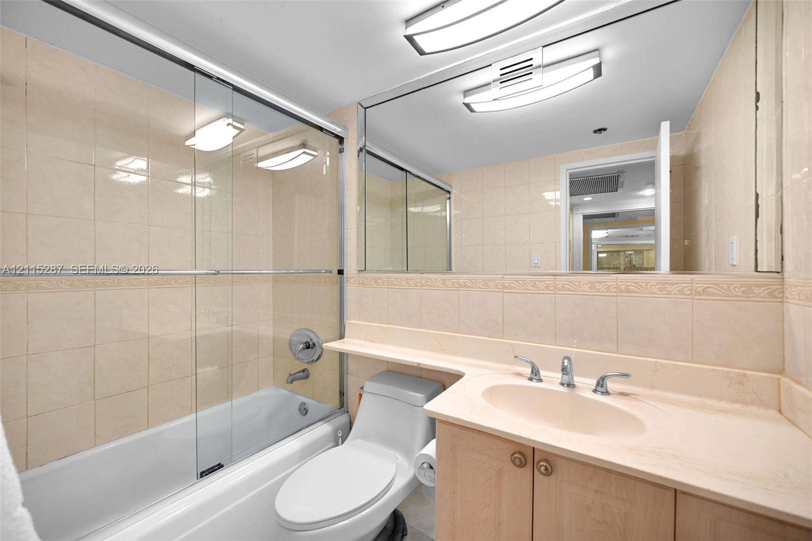 5225 Collins Avenue, #511, Miami Beach, FL 33140 Bathroom featuring floor-to-ceiling tile surround, glass shower sliding door, vanity with integrated sink and countertop, full-width wall mirror, and dual ceiling-mounted light fixtures