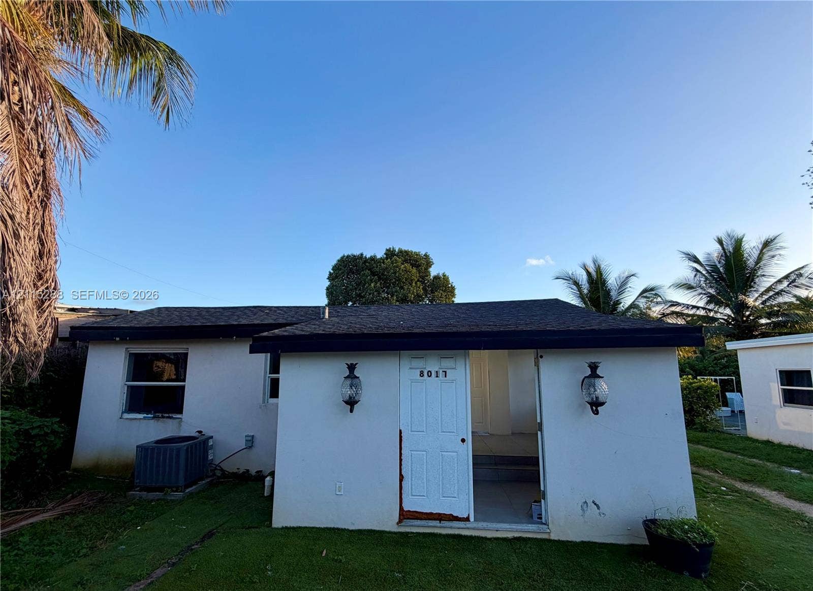 8017 NW 1st Place, Miami, Miami, FL 33150 Exterior elevation featuring stucco siding, asphalt shingle roof, dual wall-mounted coach lights, and a lawn