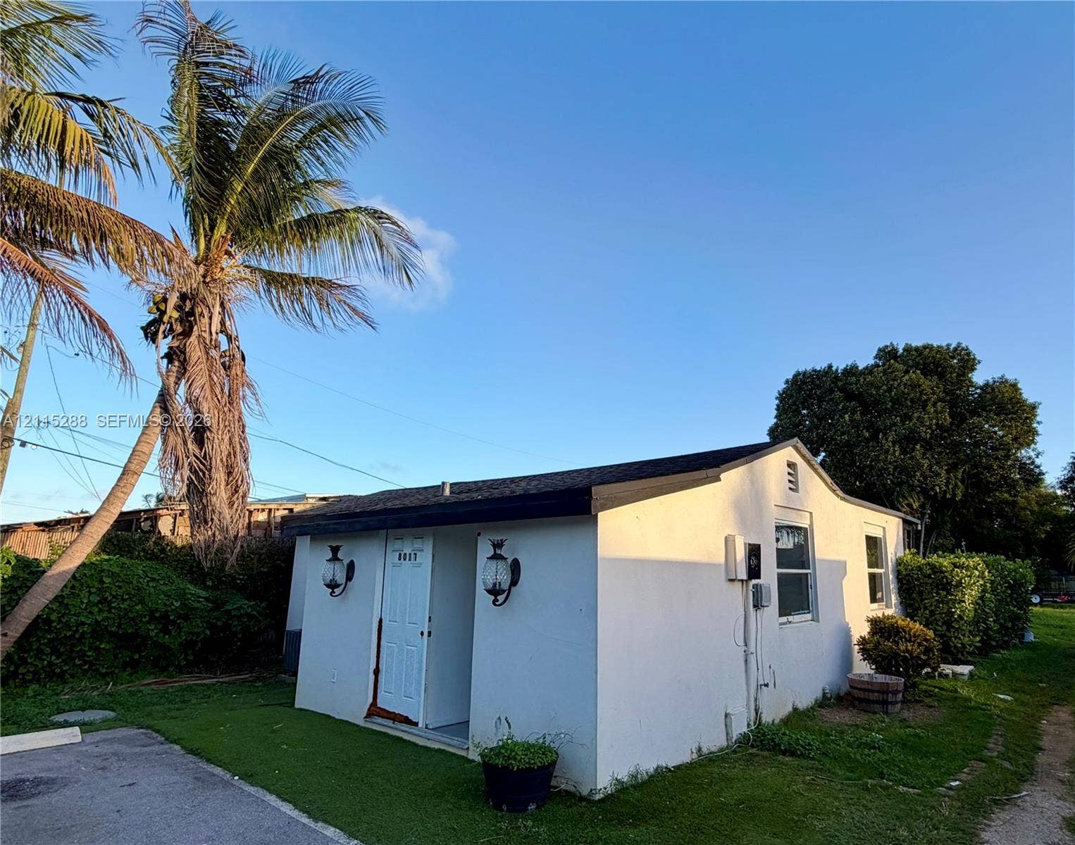 8017 NW 1st Place, Miami, Miami, FL 33150 Single-story stucco exterior featuring a gabled roof, recessed entryway, wall-mounted coach lighting, and mature palm landscaping