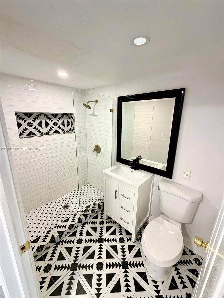 8017 NW 1st Place, Miami, Miami, FL 33150 Walk-in shower with a glass panel, recessed decorative tile wall niche, geometric patterned floor tiling, white vanity cabinet, and black-framed mirror
