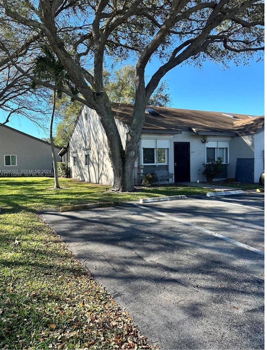 2700 SW 55th Street, #1, Dania, Dania Beach, FL 33312 Single-story exterior featuring a shingled roof, stucco siding, multi-pane windows, and a paved parking area with designated stalls