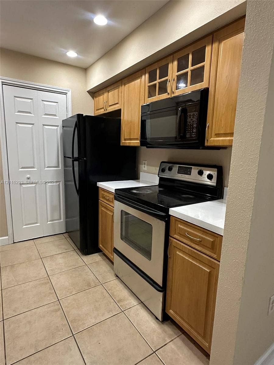 2642 NW 33rd Street, #1902, Oakland Park, Oakland Park, FL 33309 Kitchen featuring wood-finish cabinetry, solid surface countertops, a stainless steel range, a built-in microwave, and tile flooring