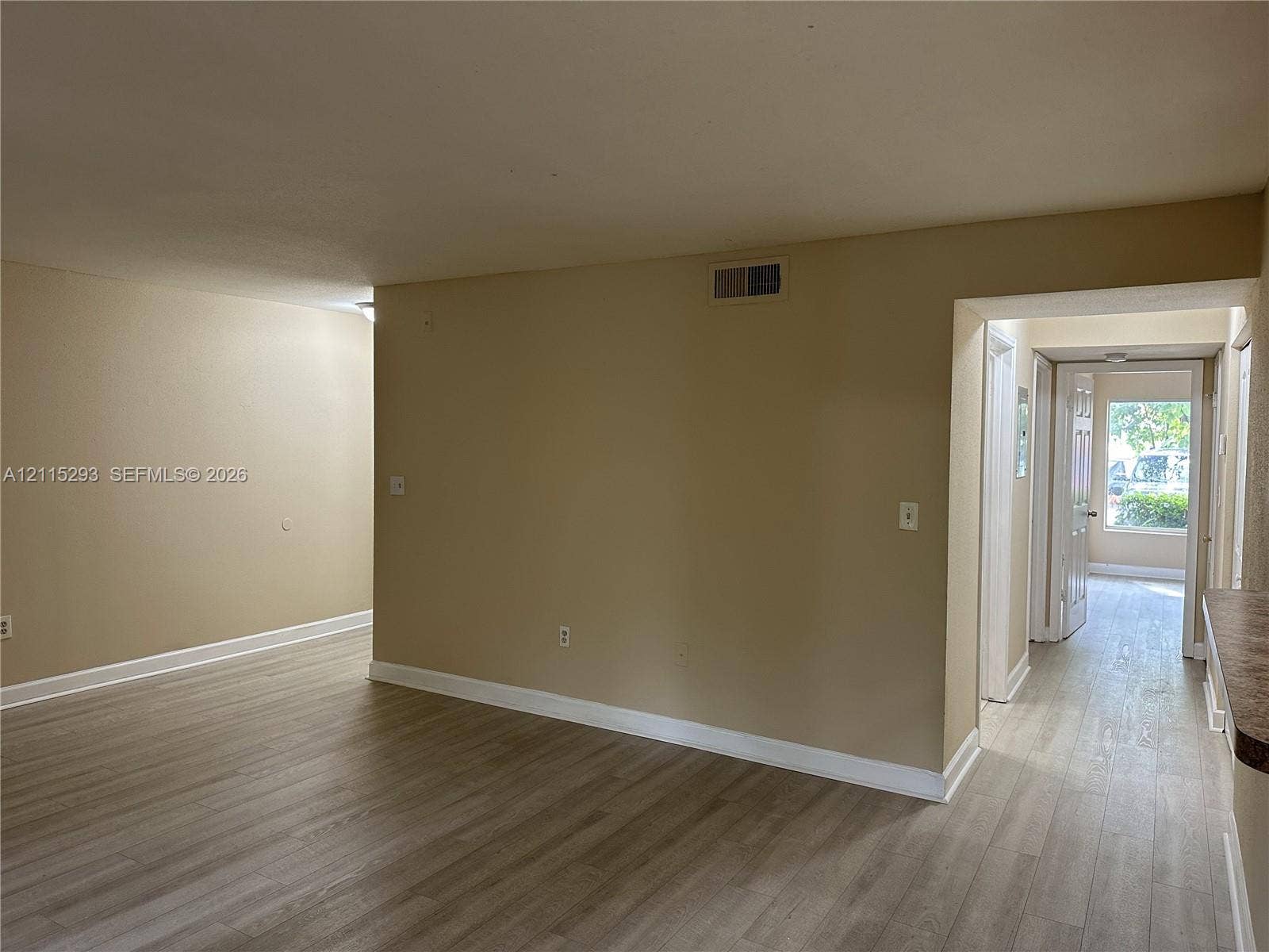 2642 NW 33rd Street, #1902, Oakland Park, Oakland Park, FL 33309 Interior space featuring wood-finish flooring and neutral wall tones, punctuated by a passage with a doorway leading to natural exterior light