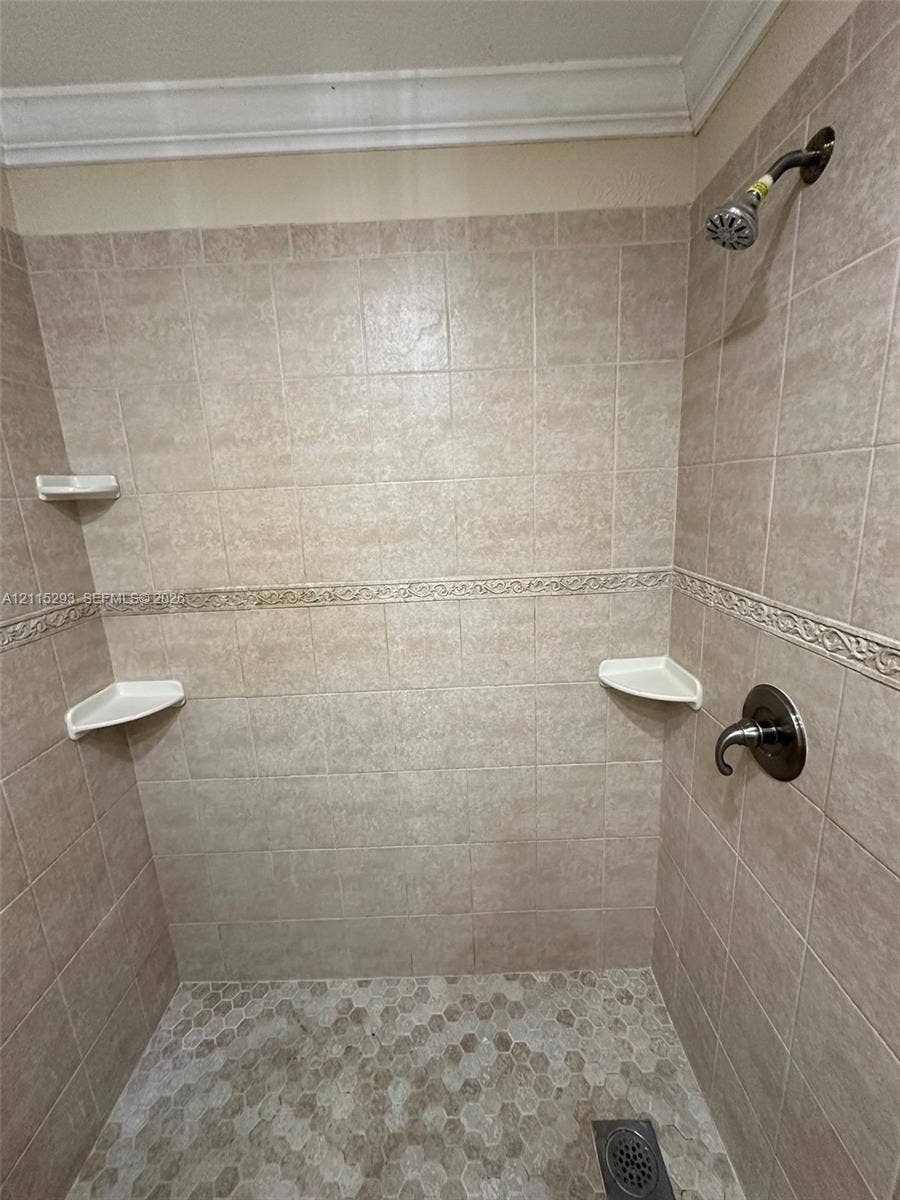 2642 NW 33rd Street, #1902, Oakland Park, Oakland Park, FL 33309 Shower enclosure featuring floor-to-ceiling tile, decorative accent trim, integrated corner shelving, hexagonal floor tiling, and wall-mounted metal fixtures