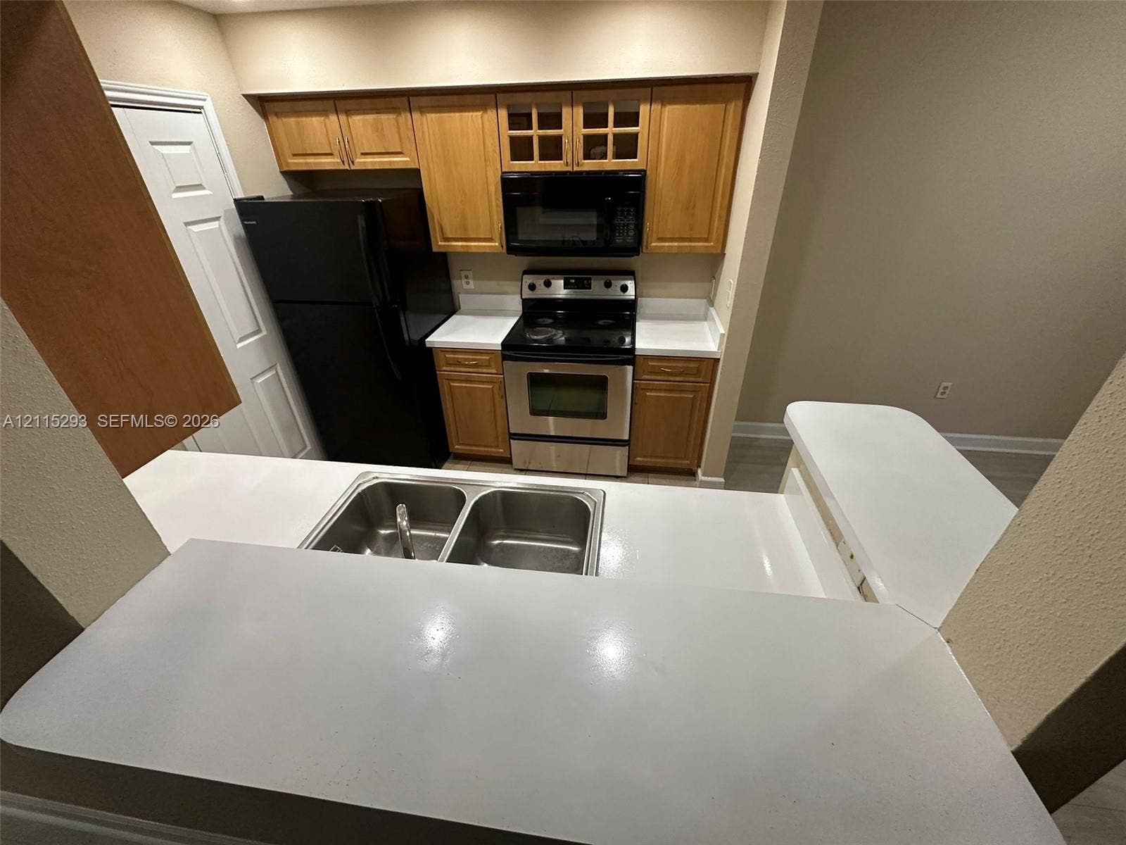 2642 NW 33rd Street, #1902, Oakland Park, Oakland Park, FL 33309 Kitchen featuring wood cabinetry, solid-surface countertops with a breakfast bar, a stainless steel electric range, and a double-basin stainless steel sink