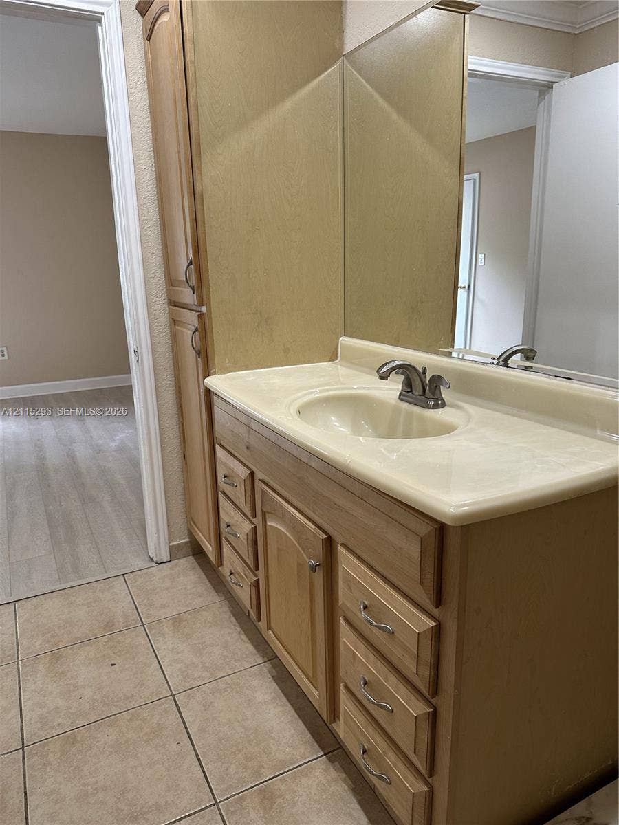 2642 NW 33rd Street, #1902, Oakland Park, Oakland Park, FL 33309 Vanity featuring light wood cabinetry, integrated storage tower, stone-composite countertop with molded sink, and a large-format vanity mirror with tile flooring