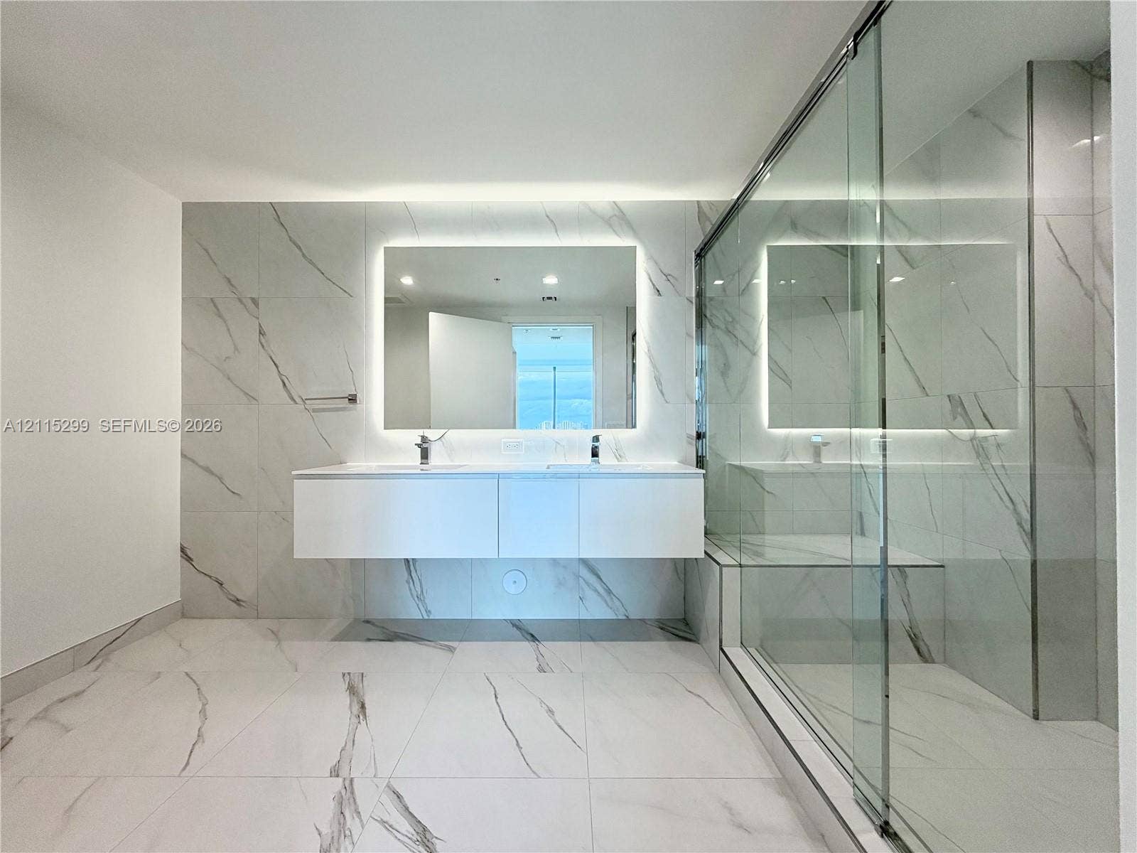 Floating dual-vanity with integrated sinks, back-lit mirror, wall-to-wall large-format tile, and glass-enclosed shower