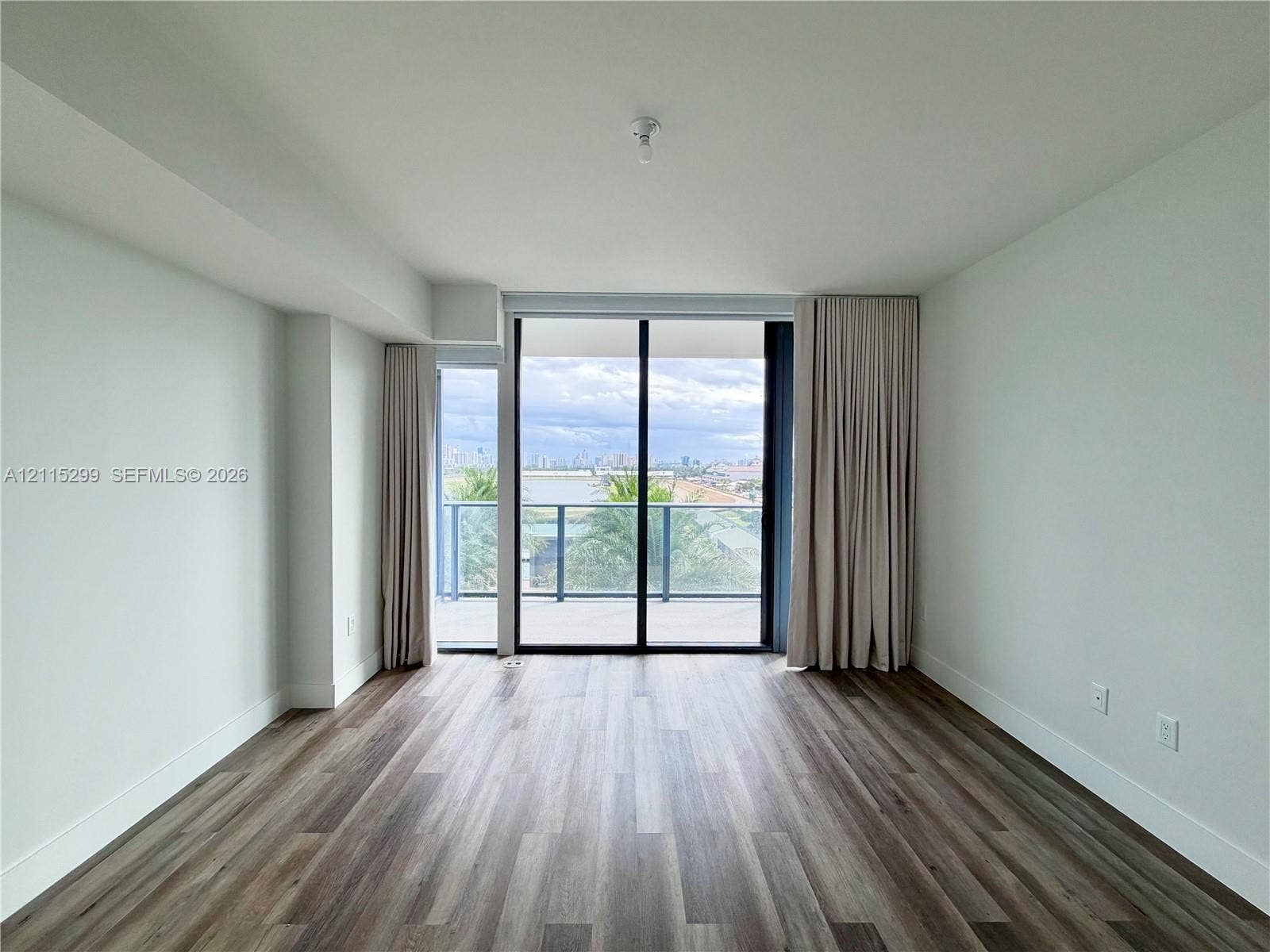 Wood-finish flooring, full-height sliding glass doors, and a private balcony with metallic railing