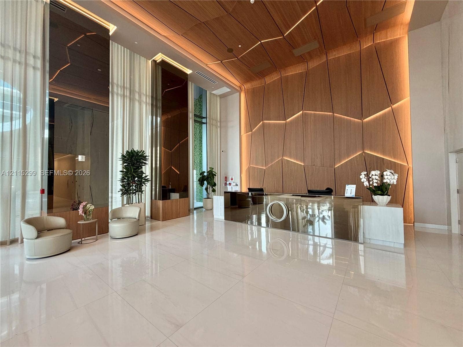 Grand lobby featuring expansive floor-to-ceiling windows, high-gloss stone tile flooring, custom wood-paneled feature wall with integrated accent lighting, and a mirrored reception desk