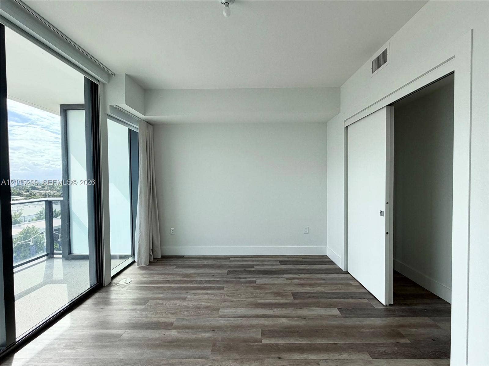 Interior space featuring wood-finish flooring, floor-to-ceiling glass paneling, a sliding door, and a balcony with a glass railing