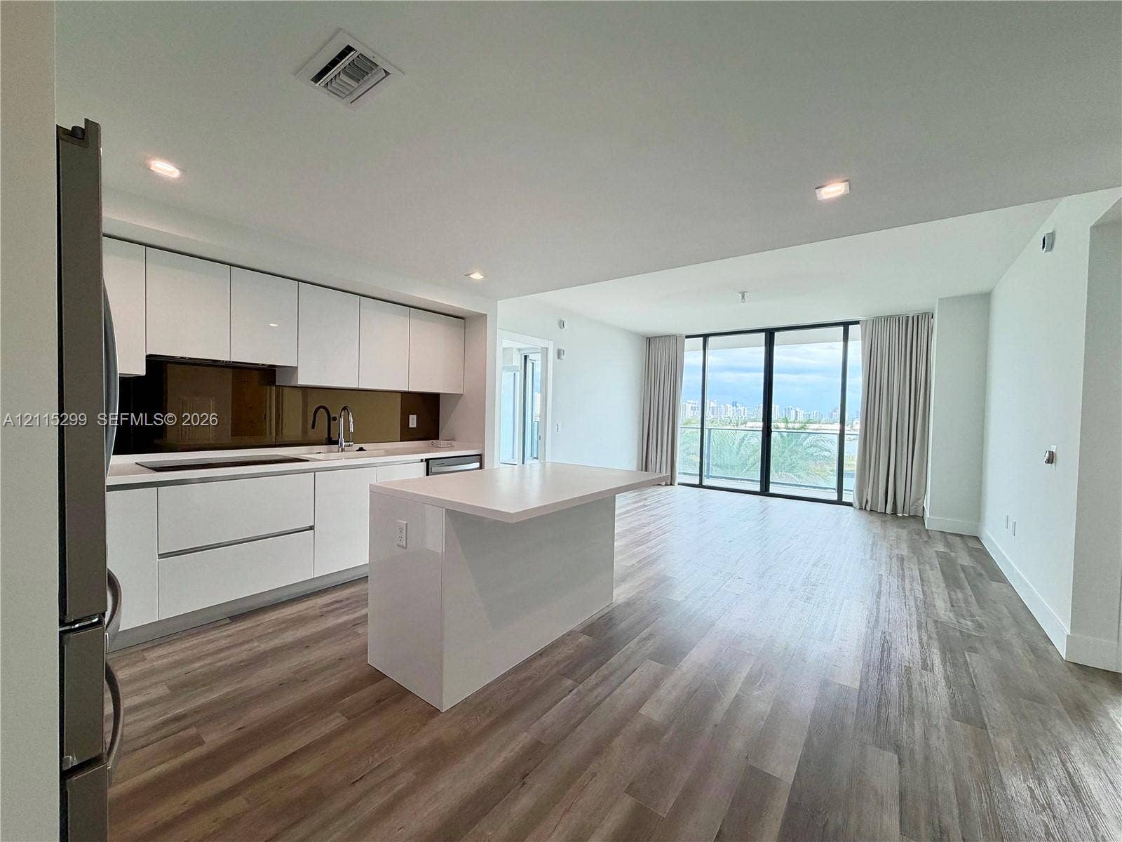 Modern kitchen featuring flat-panel white cabinetry, a center island with a stone-finish countertop, dark high-gloss backsplash, stainless steel appliances, and wood-finish flooring