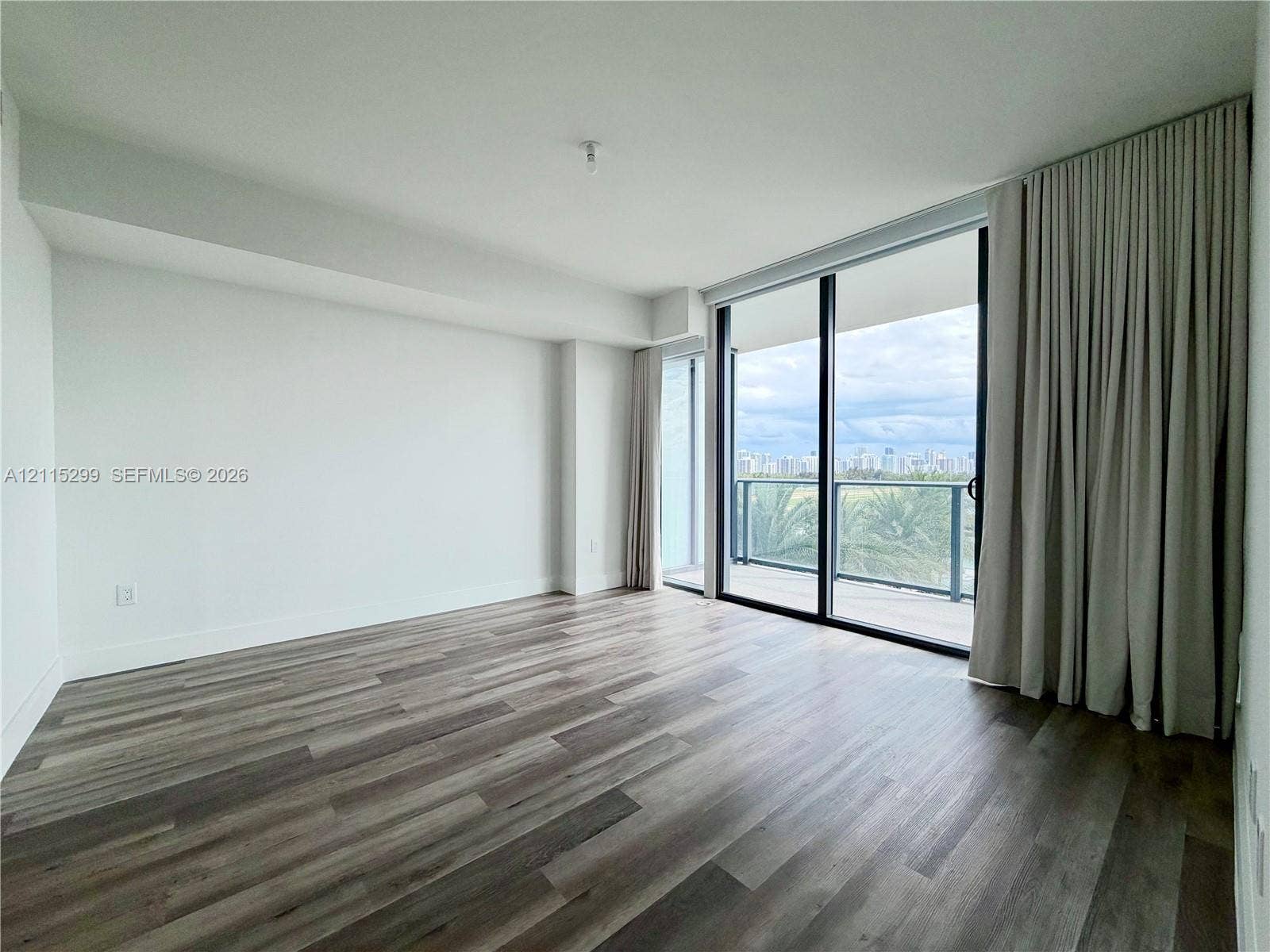 Floor-to-ceiling sliding glass doors, wood-finish flooring, and a private balcony with glass railing