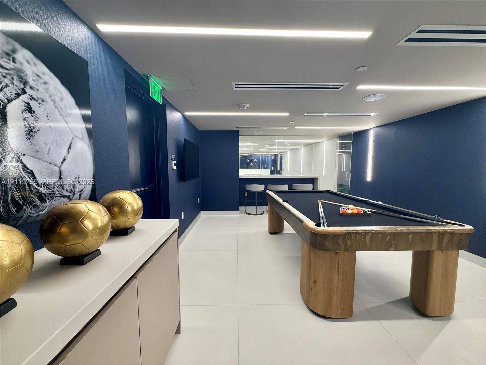 Interior space featuring large-format tile flooring, recessed linear lighting, and deep blue wall finishes, complemented by built-in cabinetry with a smooth surface countertop and a dedicated bar area