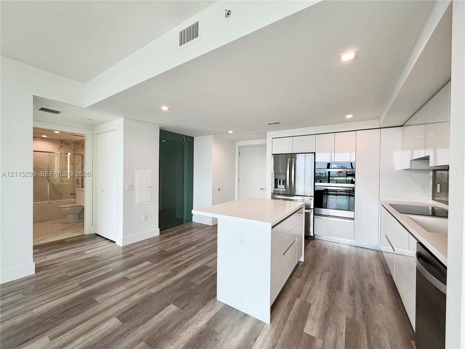 Modern kitchen featuring high-gloss cabinetry, a central island with a solid surface countertop, stainless steel appliances, recessed lighting, and wood-finish flooring