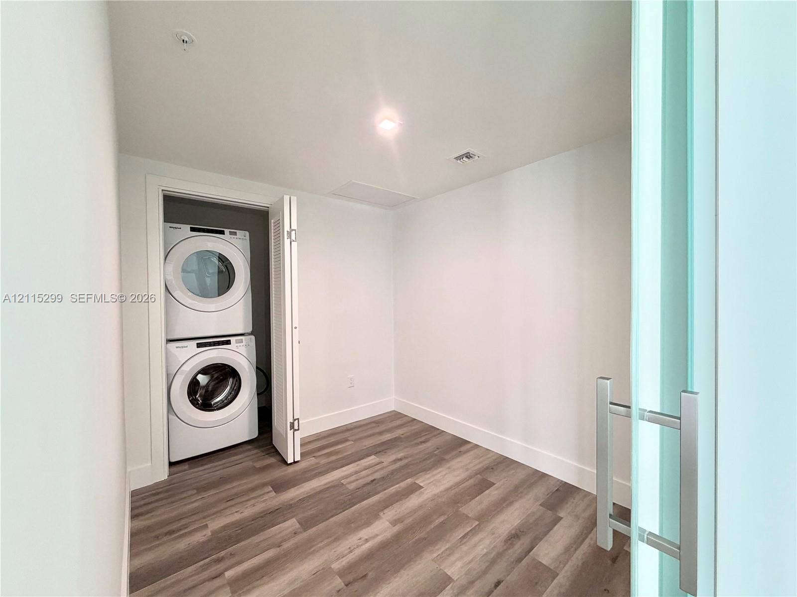 Stacked front-load washer and dryer set, wood-finish flooring, and sliding door with a metal handle