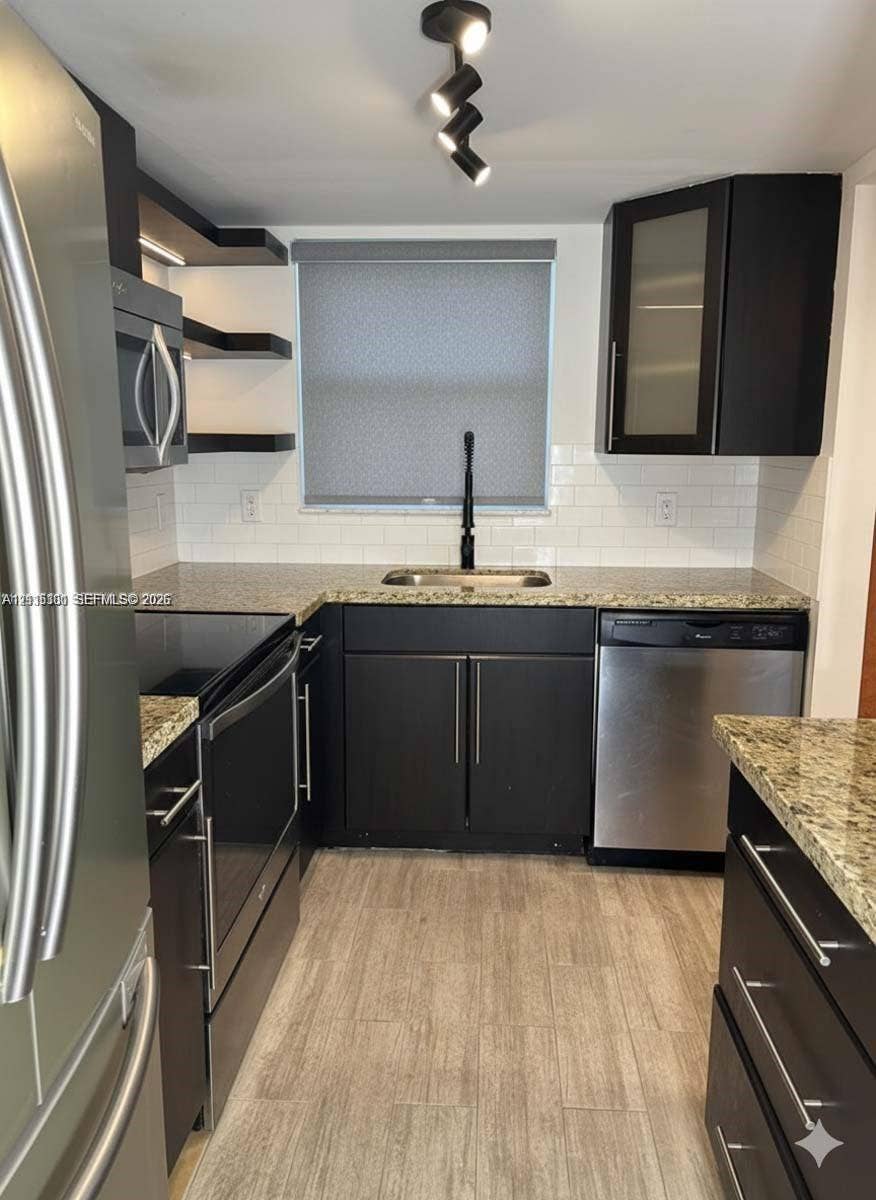 1630 Embassy Drive, #101, West Palm Beach, West Palm Beach, FL 33401 Kitchen featuring dark cabinetry, stone-finish countertops, stainless steel appliances, white subway tile backsplash, and wood-finish flooring