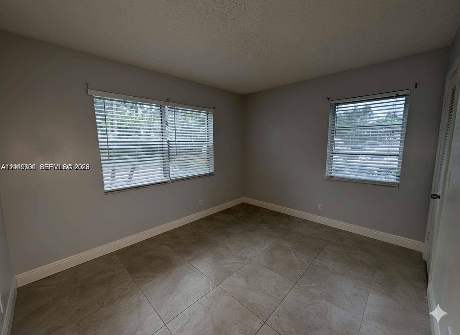 1630 Embassy Drive, #101, West Palm Beach, West Palm Beach, FL 33401 Neutral-toned interior featuring large-format tile flooring, dual windows with fitted horizontal blinds, and a louvered closet door