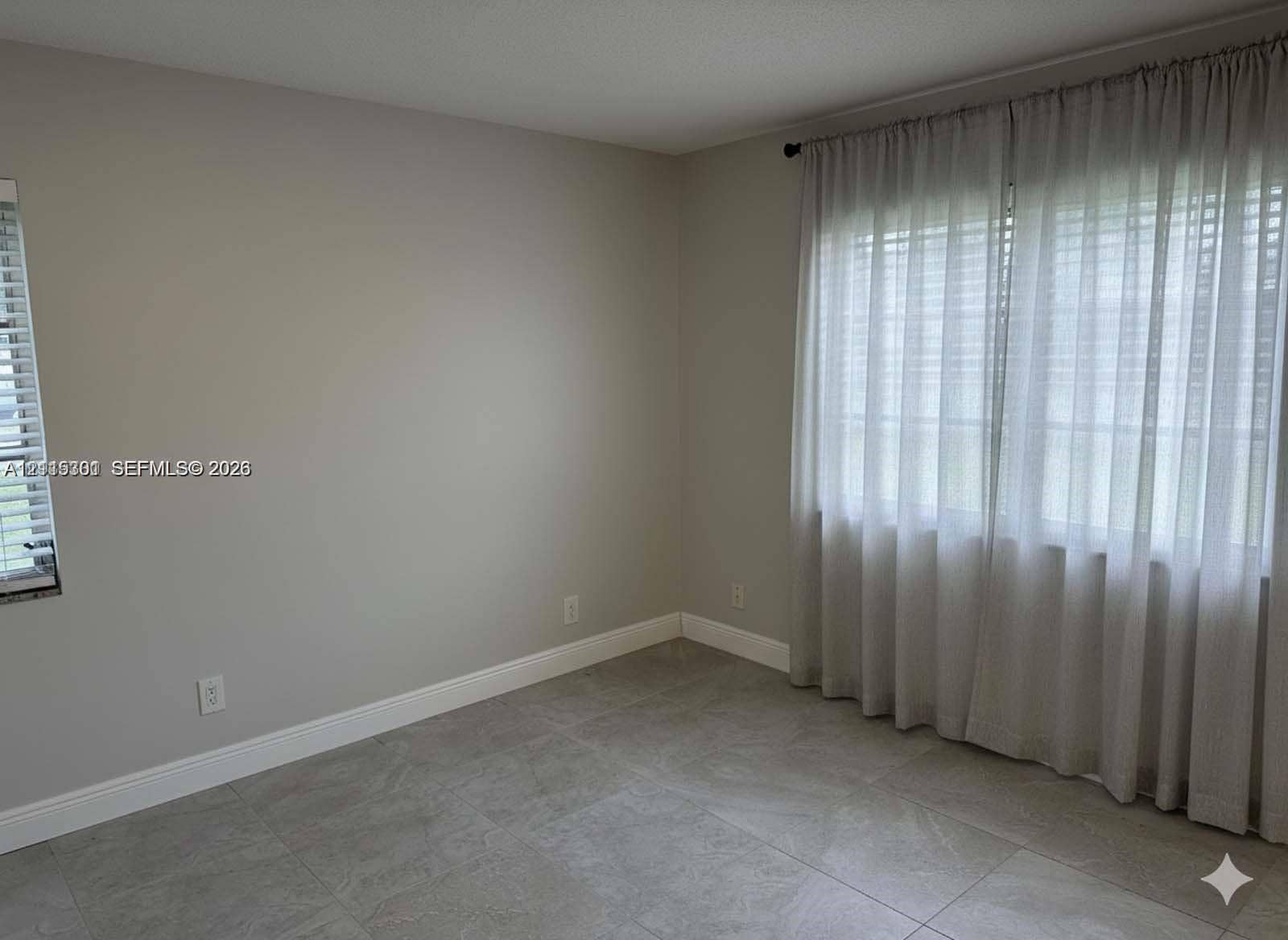 1630 Embassy Drive, #101, West Palm Beach, West Palm Beach, FL 33401 Neutral-toned interior space featuring large-format ceramic tile flooring, dual-aspect windows, and crisp wall finishes