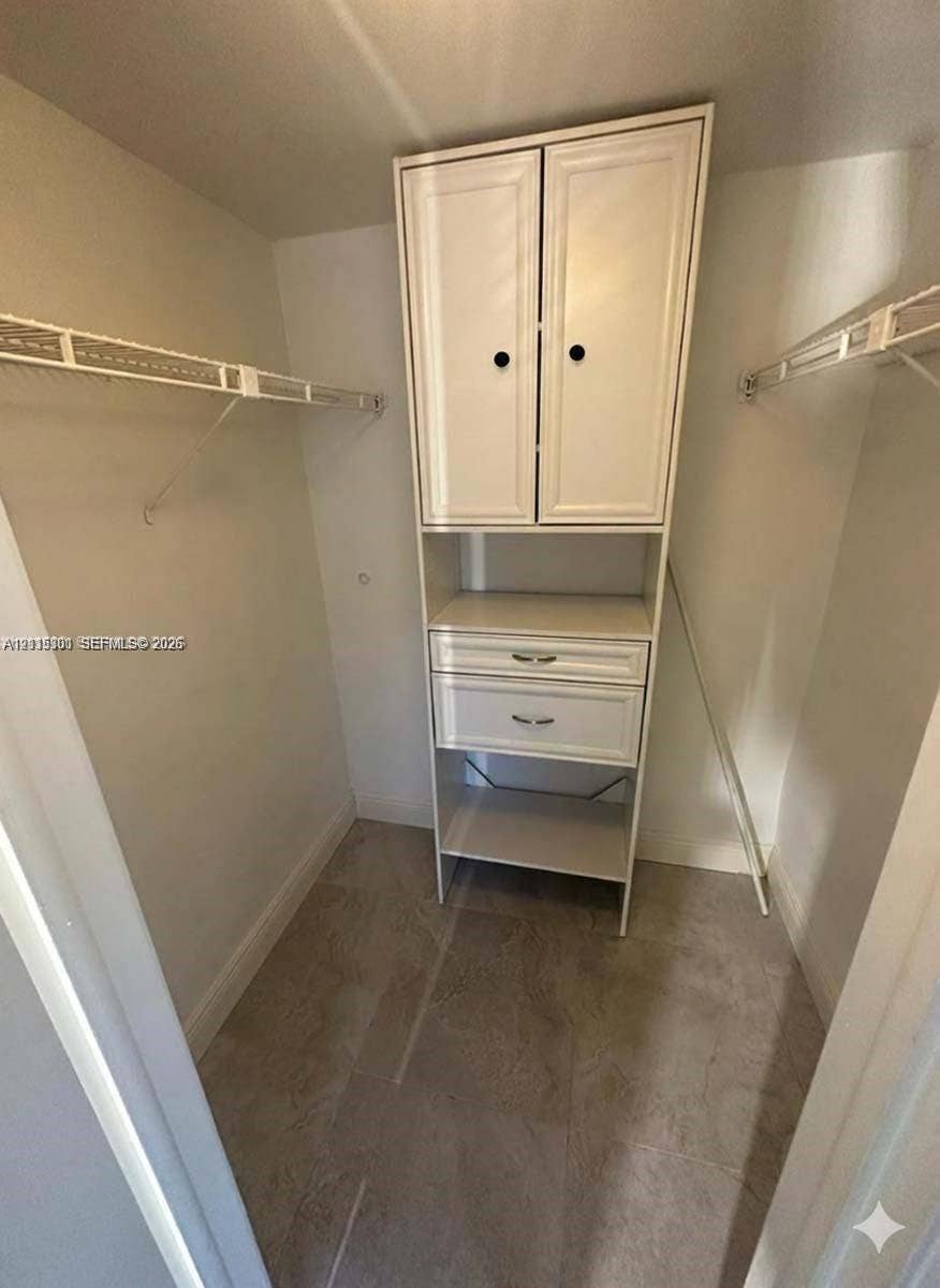1630 Embassy Drive, #101, West Palm Beach, West Palm Beach, FL 33401 Walk-in closet featuring white built-in cabinetry with two drawers and two cabinet doors, dual-level wire shelving, and neutral tile flooring