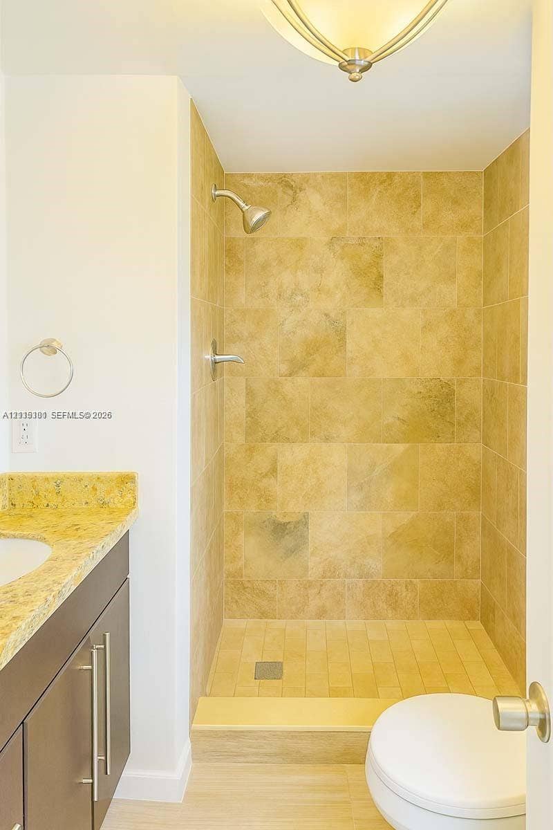1630 Embassy Drive, #101, West Palm Beach, West Palm Beach, FL 33401 Walk-in shower with stone-tile surround, dark-finish cabinetry, stone countertop with integrated sink, and polished metal hardware