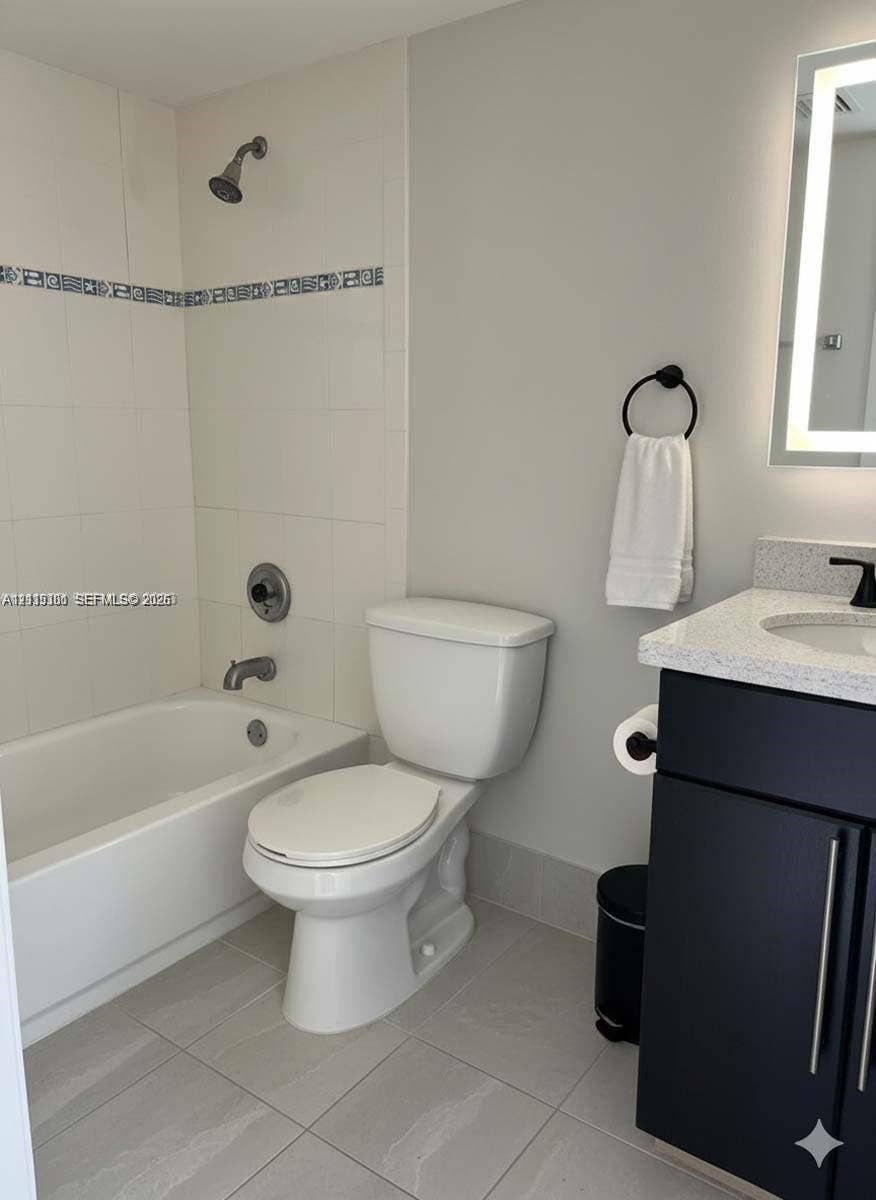 1630 Embassy Drive, #101, West Palm Beach, West Palm Beach, FL 33401 Dark cabinetry with stone-finish countertop, undermount sink, matte black hardware, and an illuminated wall mirror, complemented by a tiled shower-tub combination featuring a decorative accent border