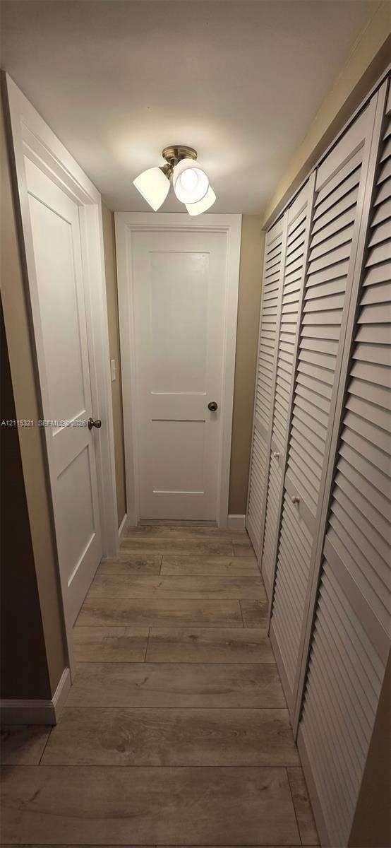 115 Lake Emerald Drive, #408, Oakland Park, FL 33309 Interior corridor featuring wood-finish plank flooring, two-panel shaker-style doors, louvered closet doors, and a multi-light flush-mount ceiling fixture