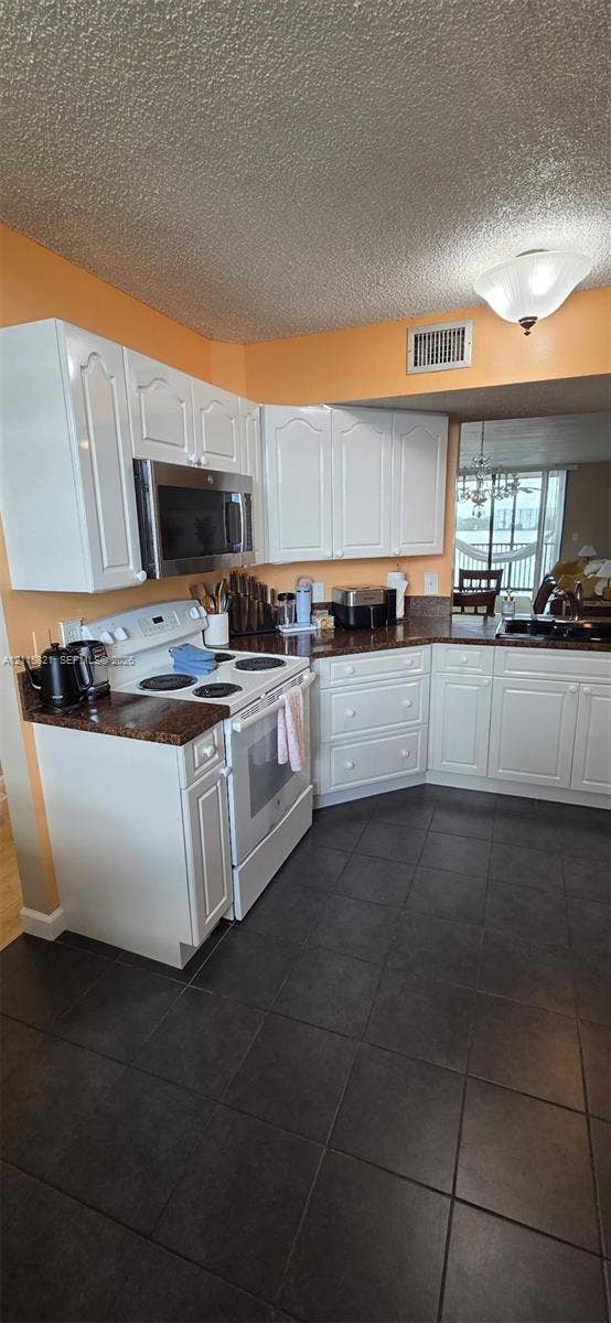 115 Lake Emerald Drive, #408, Oakland Park, FL 33309 Kitchen featuring white shaker-style cabinetry, stone-finish countertops, dark tile flooring, and integrated stainless steel microwave